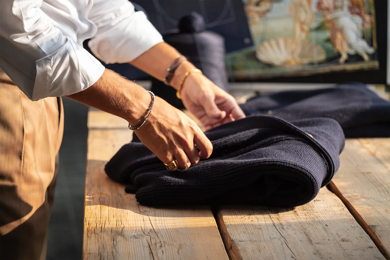 Dettaglio di un uomo in camicia bianca che piega un cardigan blu su un tavolo di legno