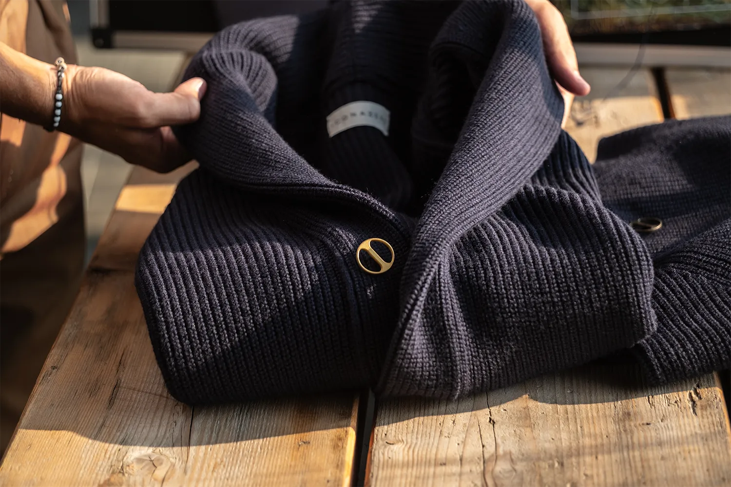 Mani che piegano un cardigan blu posizionato su un tavolo di legno